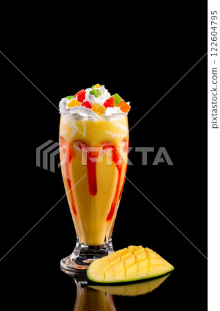 Closeup glass of mango milk shake decorated with cream and candied fruits isolated at black background. Closeup glass of mango milk shake decorated with cream and candied fruits isolated at black background. 122604795