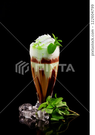 Glass of chocolate milk shake with mint and ice cubes decorated with whipped cream and syrup isolated at black background. Glass of chocolate milk shake with mint and ice cubes decorated with whipped cream and syrup isolated at black background. 122604799