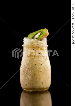 Closeup glass jar with kiwi and pear yellow fresh smoothie isolated at black background. 122604811