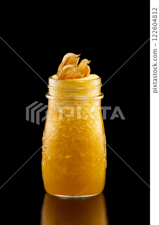 Glass jar of fresh yellow mango and orange smoothie decorated with winter cherry isolated at black background. 122604812