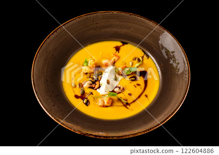 Pumpkin soup with shrimps and sour cream served in a plate isolated at black background. Pumpkin soup with shrimps and sour cream served in a plate isolated at black background. 122604886