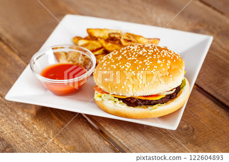 Fresh cheeseburger and potato fries with ketchup on white plate at wooden table. Fresh cheeseburger and potato fries with ketchup on white plate at wooden table. 122604893