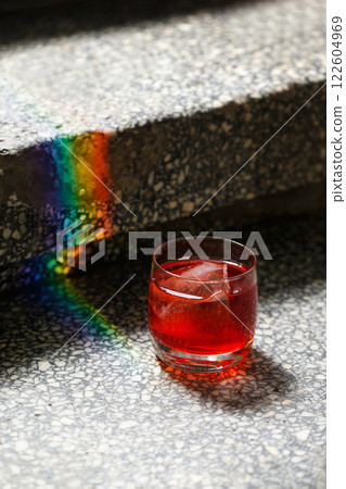 Closeup glass of negroni cocktail with ice at stairs with rainbow flare  background. Vertical image 122604969