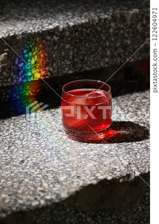 Closeup glass of negroni cocktail with ice at stairs with rainbow flare background. Vertical image with copyspace Closeup glass of negroni cocktail with ice at stairs with rainbow flare background. Vertical image with copyspace 122604971