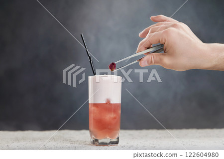 Bartender's hand is holding dry red rose decorating cocktail at grey wall background. 122604980