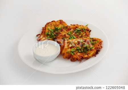 Plate of fried brown vegeterian potato pancakes with cup of cream isolated at white background. Nationail Russian meal. 122605048