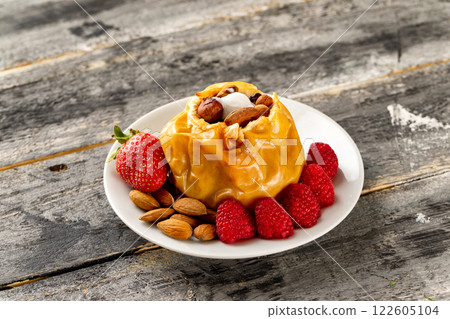 Closeup plate of stuffed baked apple dessert served with strawberries, raspberries, blueberries and nuts at wooden board background. Closeup plate of stuffed baked apple dessert served with strawberries, raspberries, blueberries and nuts at wooden board background. 122605104