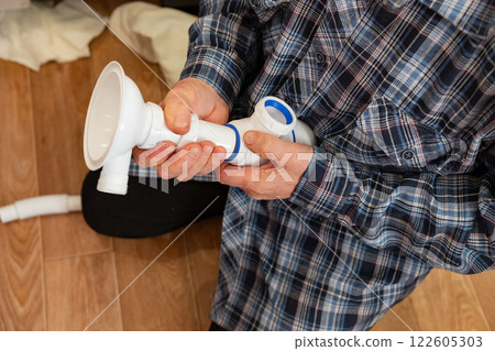 Person assembling a pipe fitting in a workshop on a wooden floor while wearing a plaid shirt 122605303