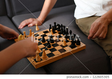 Engaging chess match between two players on a cozy couch in a living room during the afternoon Engaging chess match between two players on a cozy couch in a living room during the afternoon 122605305
