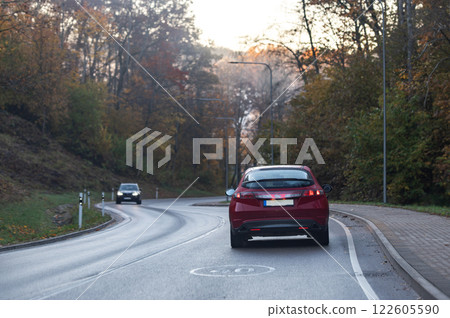 Rear view of a red car on a bend in an autumn road, speed limit sign 122605590