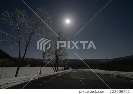 A silent winter landscape with moonlight illuminating a single road and snow A silent winter landscape with moonlight illuminating a single road and snow 122606701