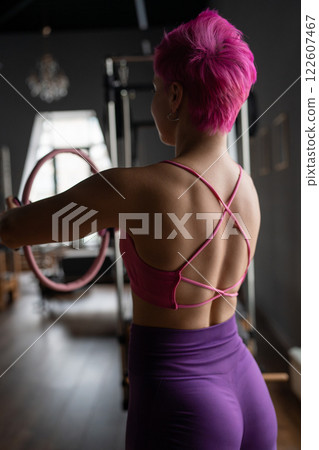 Young sporty attractive women doing pilates toning exercises for abs with flex ring toner, crunches to strengthen abdomen using pilates magic circle, and wearing sportswear in a yoga studio. 122607467
