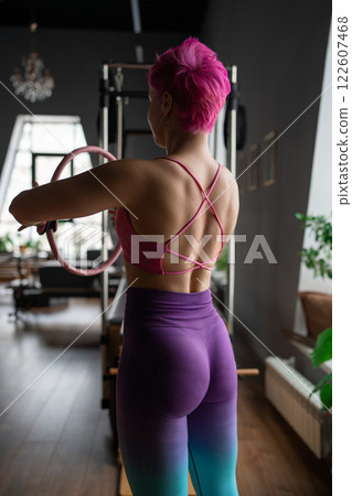 Young sporty attractive women doing pilates toning exercises for abs with flex ring toner, crunches to strengthen abdomen using pilates magic circle, and wearing sportswear in a yoga studio. 122607468