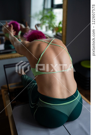 Woman doing Pilates exercise for core and back muscles on Reformer machine with determination and focus on strength body 122607578