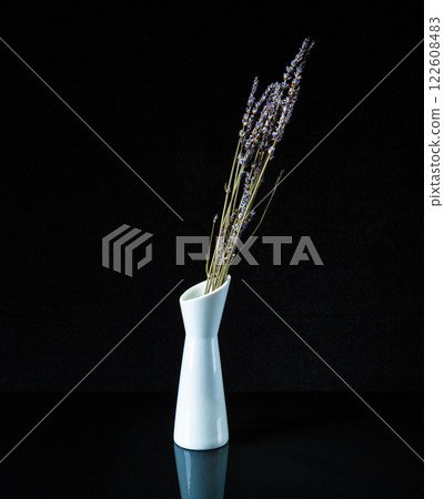a white vase with lavender flowers on a black background is reflected in a mirror stand 122608483