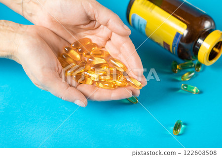 Capsules with fish oil lie in female palms on a blue background 122608508