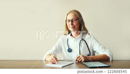 Middle-aged woman doctor sitting at desk working in clinic office Middle-aged woman doctor sitting at desk working in clinic office 122608545