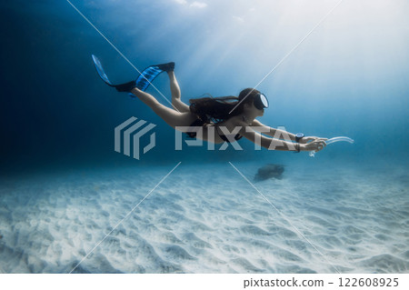 Freediver woman with diving fins glides underwater. Freediving over white sand sea bottom, activity water sport. 122608925