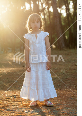Portrait of brunette child girl in white clothes standing on the background of the sunny park Portrait of brunette child girl in white clothes standing on the background of the sunny park 122609147