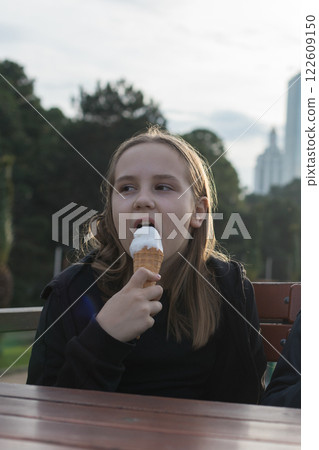 Portrait of young girl holding a vanilla ice cream in cone sitting on table 122609150