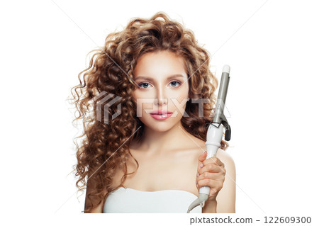 Healthy woman with curly hairstyle using hot curling tongs iron, indoor fashion portrait.  122609300