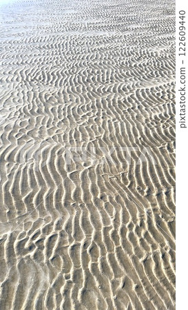 Ocean shapes sand patterns, beach texture forms wavy lines, wind sculpts sand ridges, shifting grains define ocean movement, smooth curves enhance beach texture. 122609440