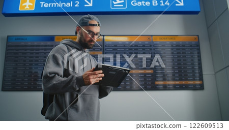 Airport Terminal: Traveler Uses Tablet Computer, Checks Flight Information on Digital Departure Board Airport Terminal: Traveler Uses Tablet Computer, Checks Flight Information on Digital Departure Board 122609513