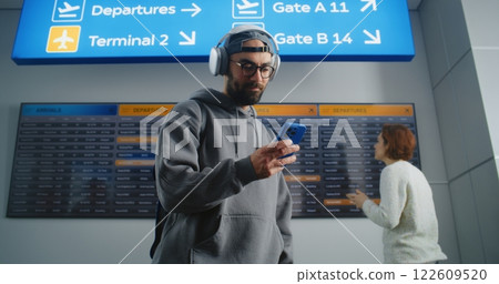 Man Checks Flight Information on Mobile Phone, Looks at Digital Arrival and Departure Board Man Checks Flight Information on Mobile Phone, Looks at Digital Arrival and Departure Board 122609520