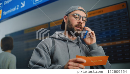 Airport Terminal: Male Passenger Holding Plane Ticket, Talking by Phone Airport Terminal: Male Passenger Holding Plane Ticket, Talking by Phone 122609564