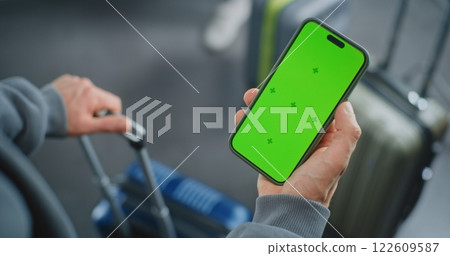 Close Up of Man Standing with Suitcase, Holding Mobile Phone with Green Chroma Key Screen 122609587