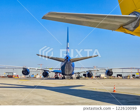 Blue passenger jet tail, seen from behind, parked on tarmac with yellow wing above. High quality photo 122610099