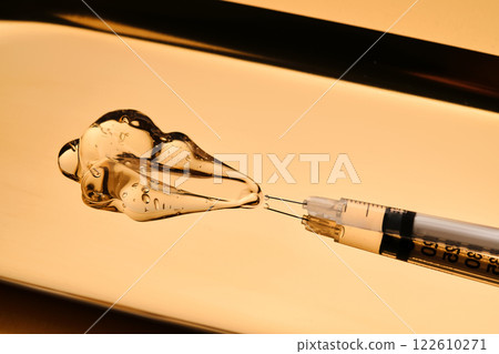 A drop of gel pours from a syringe for cosmetic procedures. 122610271