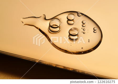 A beautiful drop of gel-like cosmetic serum with bubbles on a golden background. A beautiful drop of gel-like cosmetic serum with bubbles on a golden background. 122610275