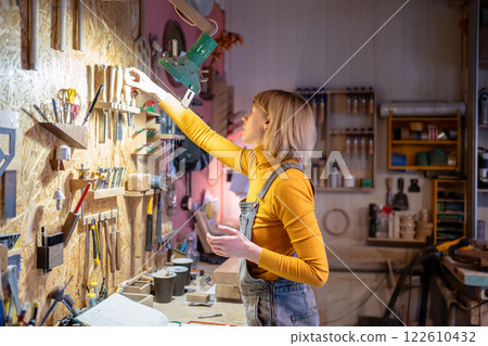 Organized efficient workspace in wooden workshop. Woman joiner organize tools, arranging workspace 122610432