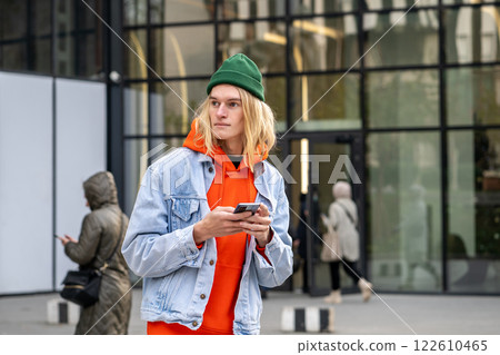 Pleased hipster guy standing outside with smartphone, looking aside, waiting friends or girlfriend 122610465