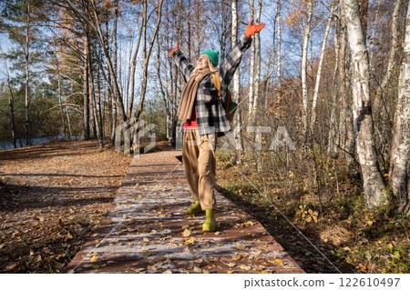 Happy woman enjoying pastime hiking in forest raising arms, breathing in fragrance of autumn air Happy woman enjoying pastime hiking in forest raising arms, breathing in fragrance of autumn air 122610497