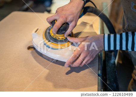 Closeup of sanding wood with orbital sander at workshop. Carpentry workshop. Furniture production Closeup of sanding wood with orbital sander at workshop. Carpentry workshop. Furniture production 122610499