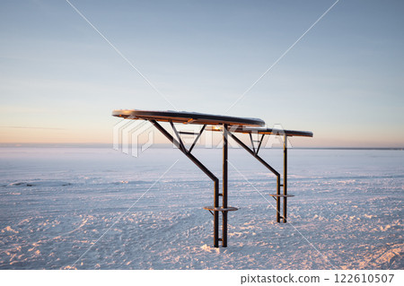 Snowy metal parasols dot empty shoreline with dramatic sky during sunrise in morning. Frosted beach 122610507