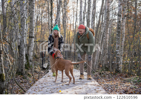 Happy family couple dog owners playing together with dog walking in autumn Scandinavian park. 122610596