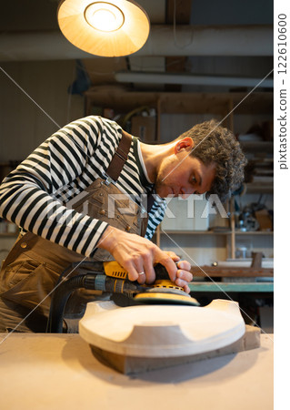 Sanding wood with orbital sander at workshop. Carpentry workshop. Furniture production 122610600