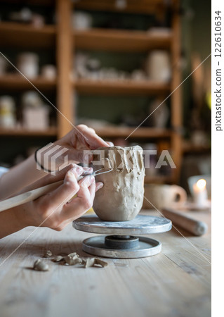 Potter hands shaping mug with loop tool, carve intricate pattern, scraping excess clay. Artisan job 122610634