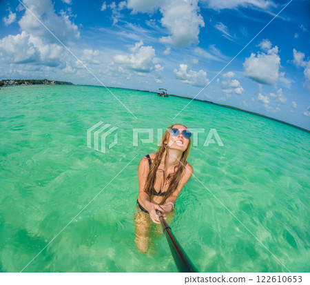 Woman standing in the crystal-clear waters of Lake Bacalar, Mexico, enjoying the serene beauty of the landscape. Tranquil moment in nature, outdoor escape, and relaxation concept 122610653