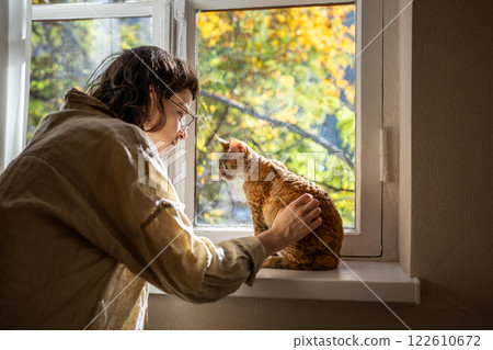 Tender pet lover stroking beloved adorable breed cat Devon Rex sitting on windowsill in sunlight Tender pet lover stroking beloved adorable breed cat Devon Rex sitting on windowsill in sunlight 122610672