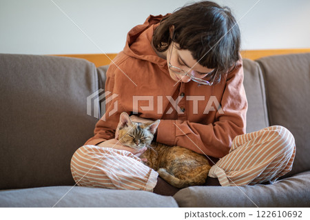 Teen girl stroking petting cat from shelter sits on sofa at home. Anti stress pet therapy, cat lover 122610692