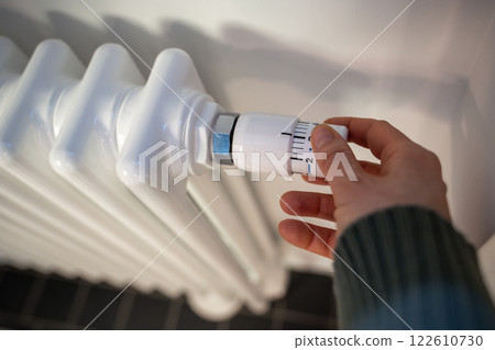 Hands adjusting radiator regulator, increasing temperature in house. Cold at home in winter season 122610730