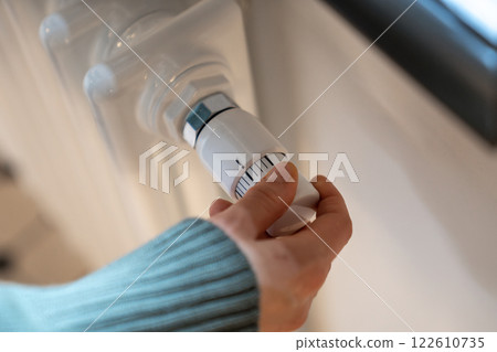 Hand turning radiator valve reducing temperature in flat, private house to save, economize energy 122610735