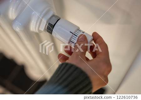 Woman regulates heating on battery radiator at home in cold season, hands close-up. Woman regulates heating on battery radiator at home in cold season, hands close-up. 122610736