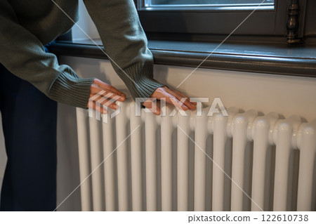 Woman warming hands near radiator at home after walking in cold winter weather, closeup Woman warming hands near radiator at home after walking in cold winter weather, closeup 122610738