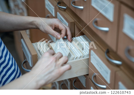 Woman student finding book cards in university card index catalog in library.  122610743