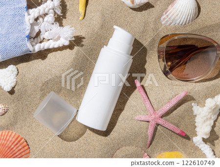 Sunscreen bottle near towel, starfishes and seashells on sand top view, hand shadow, cosmetic mockup 122610749